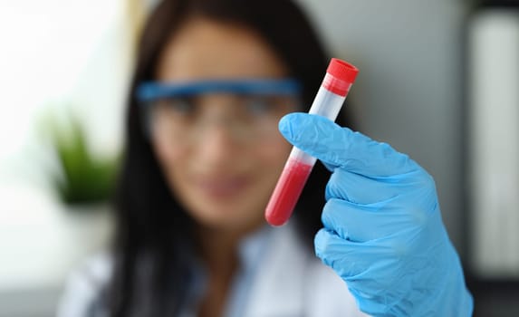 Female hand in blue protective gloves holding test tube with red liquid closeup