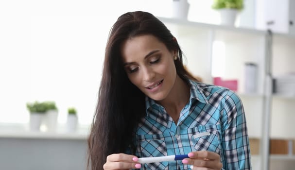 Girl has feeling surprise looking at pregnancy test. Conscious desire parents. Girl holds test with two stripes in her hands and has slight concern. Wife make pregnancy test at home