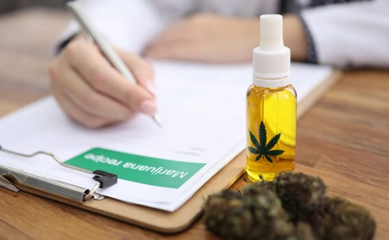 On table is hemp and marijuana oil, doctor writes. Narcotic and psychotropic drugs. Hemp blossom and hemp oil. Cannabis prescription. Cannabidiol relieves anxiety, irritability and depression
