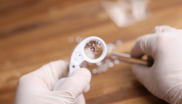 Close-up view of person looking on pink diamond through magnifying loupe. Professional in protective gloves working with precious stone. Luxury jewelry concept