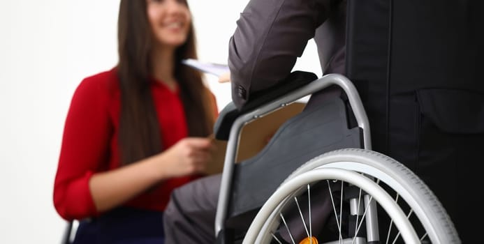 Close-up view of smiling businesswoman interviewing disabled candidate in office. Male in disabled carriage. Adaptation of people with disabilities in society concept