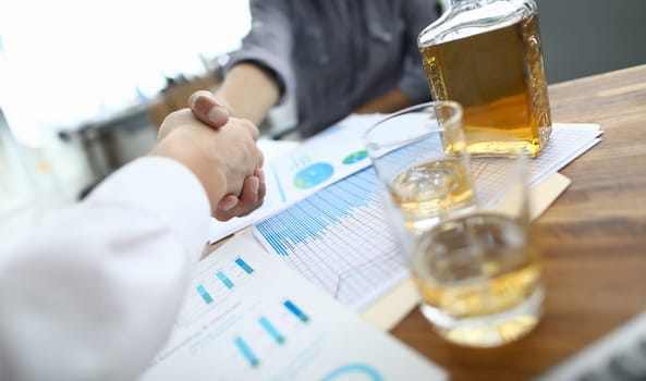 Close-up view of businessman handshaking after making good deal. Partners celebrating signing important agreement in office. Business meeting and negotiations concept