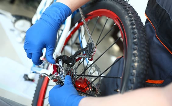 Close-up view of mechanic hands repairing mountain bike in workshop. Macro shot of bicycle wheel. Special equipment for transport maintenance. Improvement and vehicle concept