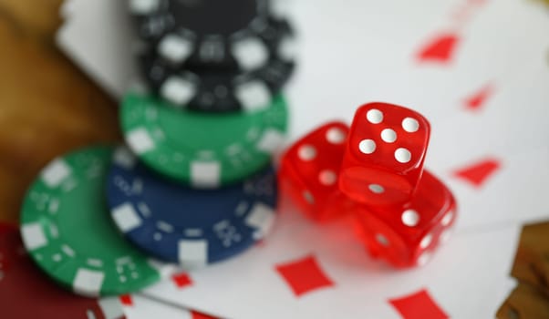 Close-up view of red dice laying on table. Macro shot of colourful casino chips on playing cards. Gambling and entertainment concept. Poker and games of chance