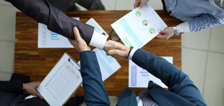 Top view of men shaking hands in office. Business meeting on important discussion. Workplace with papers with diagrams and charts. Good deal and celebration concept