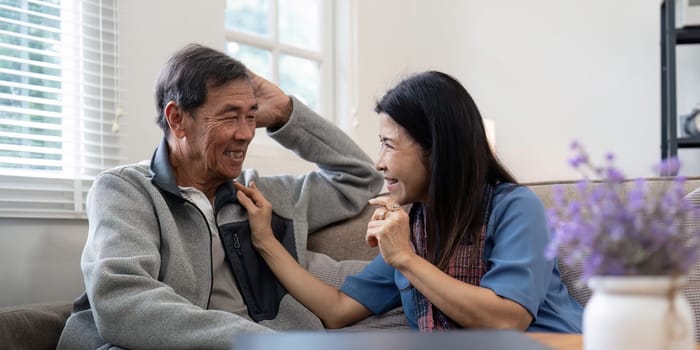 Happy mature husband and wife sit rest on comfortable sofa in living room enjoy talking, smiling elderly couple relax on couch at home chat speak laugh on leisure weekend.