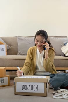 Woman asian preparing a delivery box with her used clothes, Donation and recycling concept.