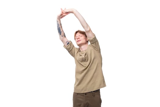 a young European guy with red hair is dressed in a fashionable beige shirt and brown trousers doing exercises.