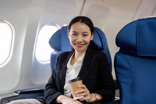 Portrait of A smiling successful Asian businesswoman or female entrepreneur in formal suit in a plane sits in a business class seat during flight.