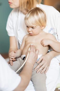 Small child being checked for heart murmur by heart ultrasound exam by cardiologist as part of regular medical checkout at pediatrician