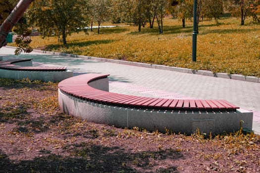 Close-up of a brown wooden bench in the shape of an arc in a summer city park, pink tinted.