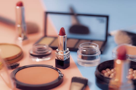 One red lipstick on a pink-blue background with a blurry set of female cosmetics, close-up side view with depth of field. The concept of cosmetics, beauty salon.