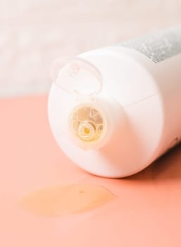 One white bottle with shampoo flowing out of it lies on a white-peach background close-up side view. The concept of cosmetics, isolation, personal hygiene.
