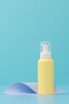 One yellow bottle with a dispenser and a transparent cap lid stands on a curved pale lilac paper on a light blue background, close-up side view.Cosmetics concept.