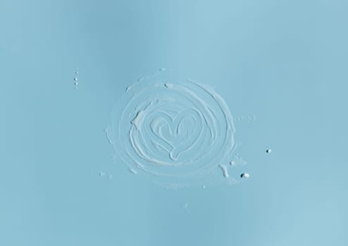 One round snail white smear of gel with a heart in the middle is located in the center on a blue background, flat lay close-up.
