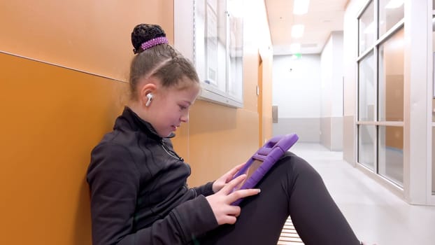 Nestled in a quiet hallway, this dedicated young figure skater finds a moment of tranquility, engrossed in her tablet as she mentally prepares for her upcoming performance.