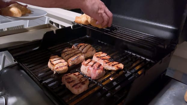 Fresh pork chops are graced with the perfect blend of seasoning as they cook to perfection, with hints of golden sear marks from the heat of an outdoor gas grill.