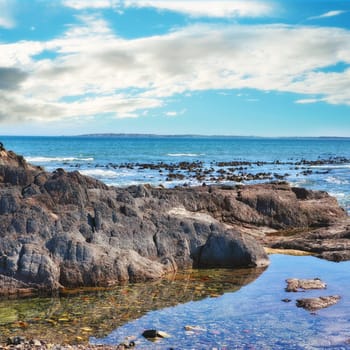 Rocks, sea and landscape with nature, blue sky and clouds with coastline and outdoor travel destination. Surf, Earth and water with ocean view, natural background and beach location in Cape Town.