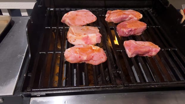 Fresh pork chops are graced with the perfect blend of seasoning as they cook to perfection, with hints of golden sear marks from the heat of an outdoor gas grill.