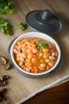 beans stewed with vegetables, mushrooms and spices, in a bowl, on a wooden table. AI generated image.