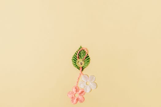 One beautiful homemade martisor made from flowers, a petal and a cheerful smiley face lies at the bottom in the center on a gentle yellow background with copy space on the sides, flat lay close-up.