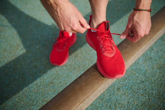 View from above of a sportsman tying shoe laces, getting ready for morning run on urban environment. Young active man running jogging exercising in the park. Fitness, healthcare and dieting concept