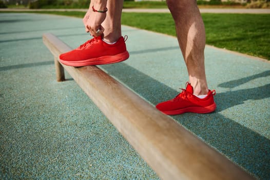 Closeup of a guy fixing his red sport shoes before training at park or running, jogging, sprinting. Footwear. Sports shoes. Active lifestyle