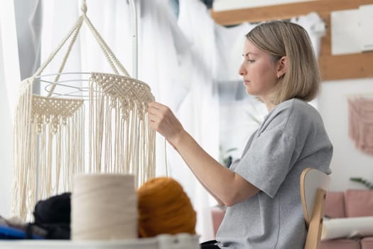 Woman making macrame lampshade using white cord to tie the strings together. Woman knits lampshade for interior using macrame technique. Woman knits boho chandelier at home