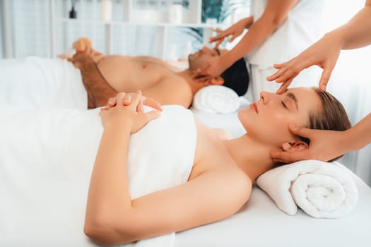 Caucasian couple enjoying relaxing anti-stress head massage and pampering facial beauty skin recreation leisure in dayspa modern light ambient at luxury resort or hotel spa salon. Quiescent