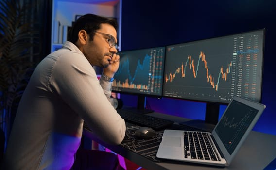 Smart trader businessman concentrating on dynamic stock exchange investment on pc and laptop showing on screen with high profit in searching market at neon light office in dark room night. Surmise.