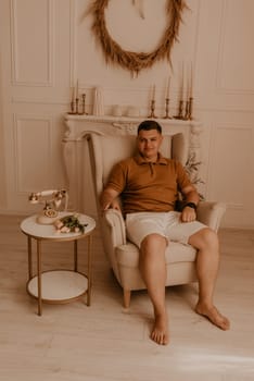 successful adult smiling man sitting in chair and looking at camera friendly. modern designer interior in beige pastel colors. Ukrainian young family. romantic, gentle, stylish photo session