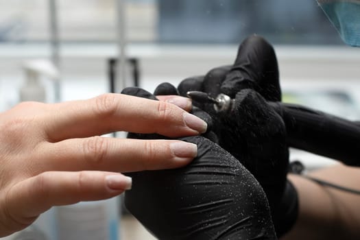 Beauty concept. A manicurist in black latex gloves makes a hygienic manicure and paints the client's nails with gel polish in a beauty salon. Close-up.