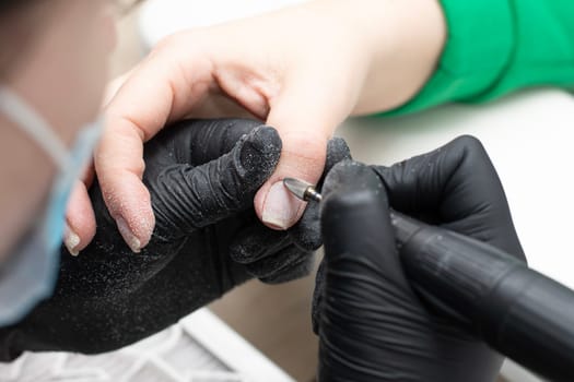 Beauty concept. A manicurist in black latex gloves gives a client a hygienic manicure and removes the cuticle on her nails with a Fraser in a beauty salon. Close-up. Horizontal.