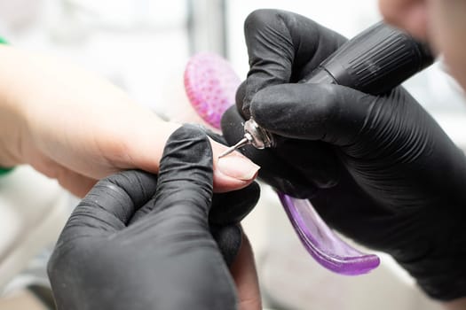 Beauty concept. A manicurist in black latex gloves makes a hygienic hardware manicure with a Fraser to a client in a beauty salon. Close-up. Horizontal.