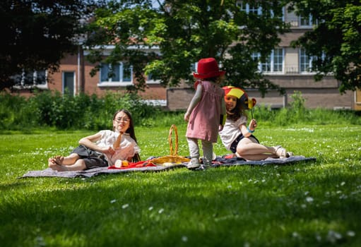 Portrait of three beautiful caucasian girls sitting on a gray bedspread with Belgian flag,basket,drinks, chips with crackers and party decorations on the lawn in the park on a sunny spring day, close-up side view.