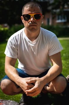 Portrait of a handsome young caucasian man wearing belgian flag sunglasses celebrating belgium day at a picnic in a city park on a sunny summer day.