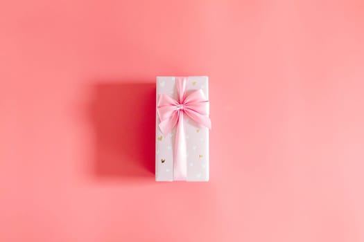 One beautiful gift box with a bow lie in the center on a bright pink background with copy space on the sides, flat lay close-up.