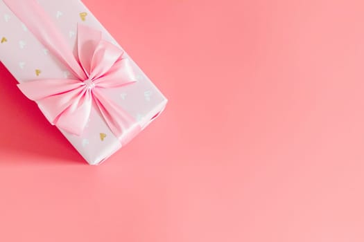 One beautiful gift box with a bow lie on the top left on a pale pink background with copy space on the right side, flat lay close-up.