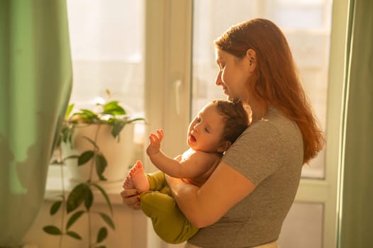 Caucasian woman tenderly holds her newborn son while standing near the window