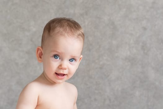 A smiling baby without a shirt is looking at the camera