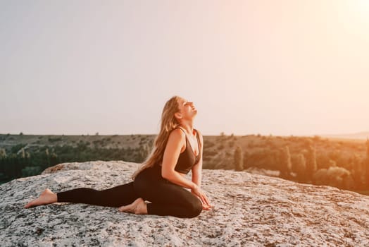 Well looking middle aged woman with long hair, fitness instructor in leggings and tops doing stretching and pilates on the rock near forest. Female fitness yoga routine concept. Healthy lifestyle.