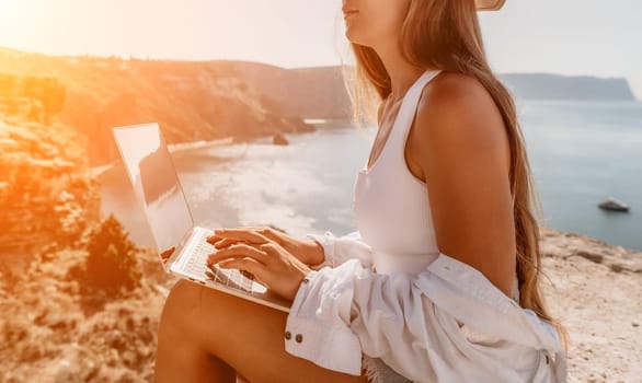 Digital nomad, Business woman working on laptop by the sea. Pretty lady typing on computer by the sea at sunset, makes a business transaction online from a distance. Freelance remote work on vacation