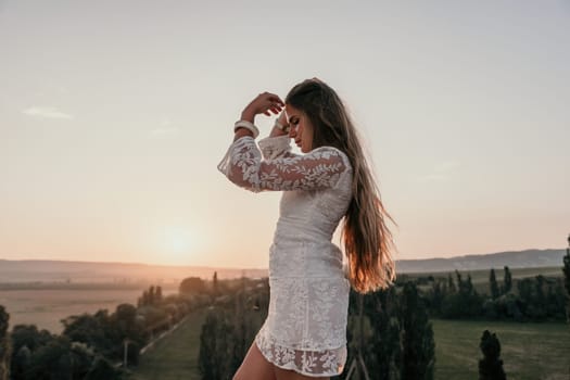 Romantic beautiful bride in white dress posing with sea and mountains in background. Stylish bride standing back on beautiful landscape of sea and mountains on sunset