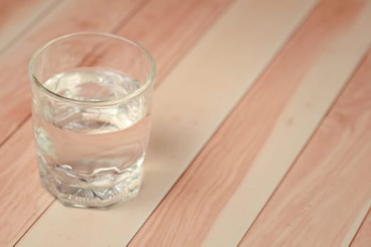 A clear glass filled with water on a wooden table for a refreshing and health-conscious beverage. Soft focus image.