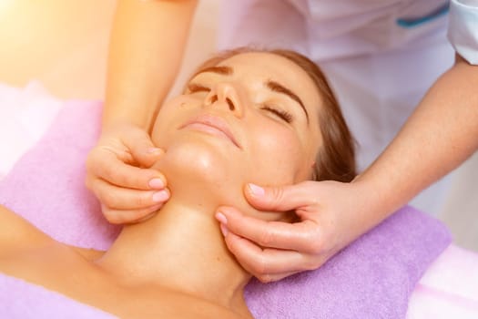 Relaxing massage. European woman getting facial massage in spa salon, side view.