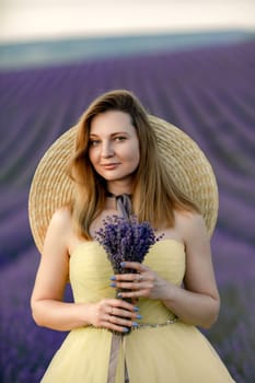 Woman poses in lavender field. Happy woman in yellow dress holds lavender bouquet. Aromatherapy concept, lavender oil, photo session in lavender.