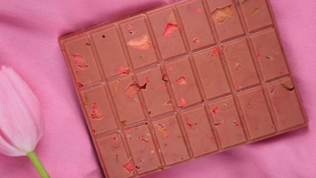 A bar of pink ruby chocolate with sublimated freeze-dried strawberries and almonds and spring tulip flowers . A dessert based on berries and nuts for International Women's Day, March 8, mother's day