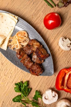 Juicy meat kebab with vegetables and herbs on a wooden table. view from above.