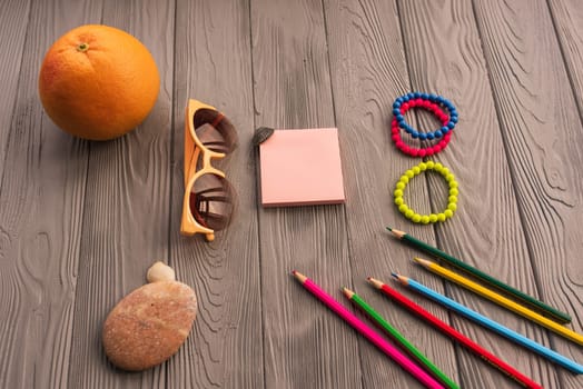 artist pencils for inscription. accessories sunscreen spf care. sunglasses bracelets orange fruit pebbles. Summer background template mockup space colorful composition text. Top view wooden background