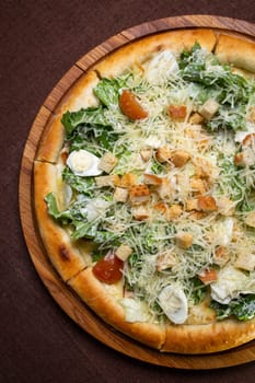 A delicious round pizza with salad, tomatoes, cheese, croutons on wooden board. Isolated on brown background, perfect for food blogs, restaurant websites, social media.